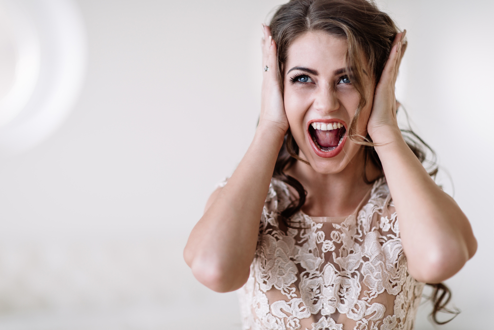 Angry bride in wedding dress covering her ears yelling at someone