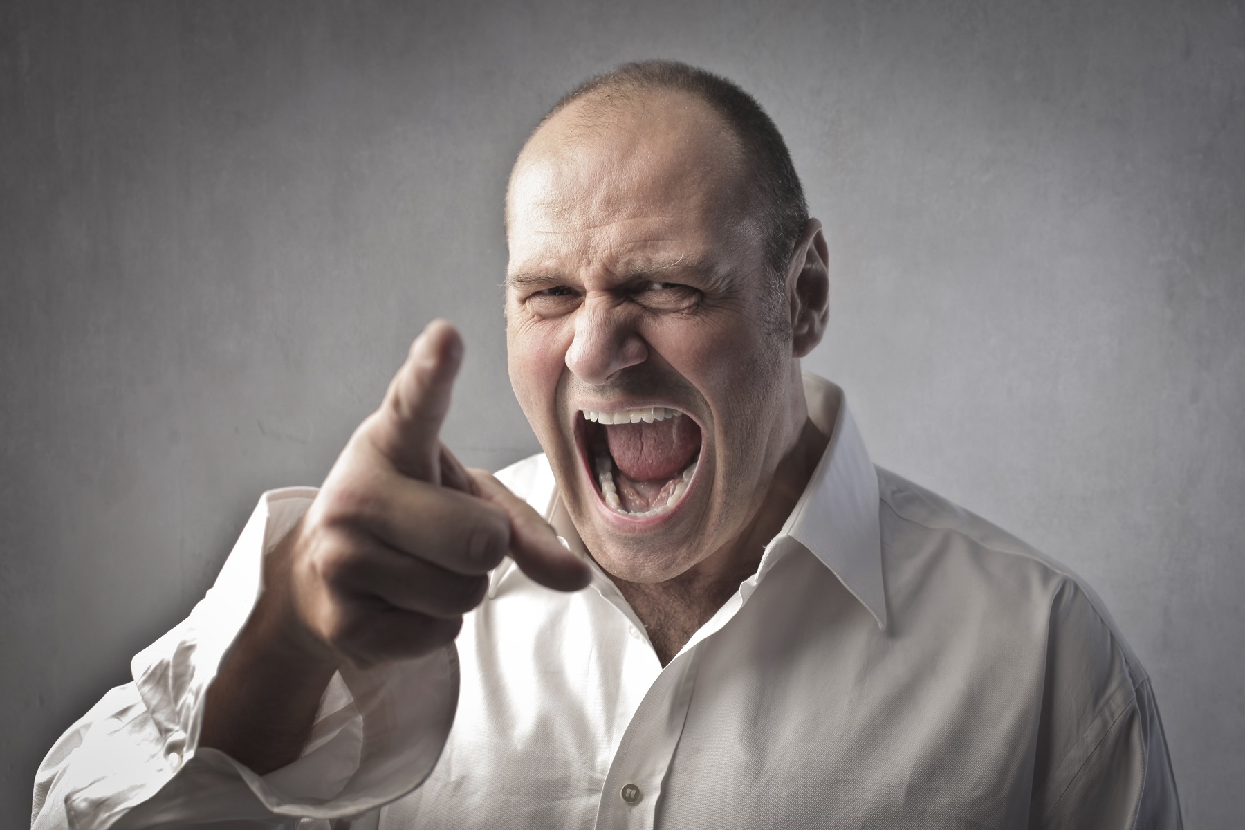 Angry man wearing white shirt is shouting and pointing with finger.