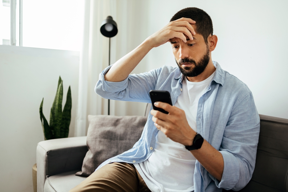 Shocked  man checking smartphone sitting on a sofa at home