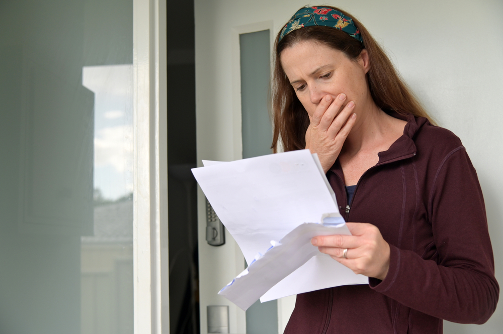 Shocked adult woman reading a letter outside a home front door