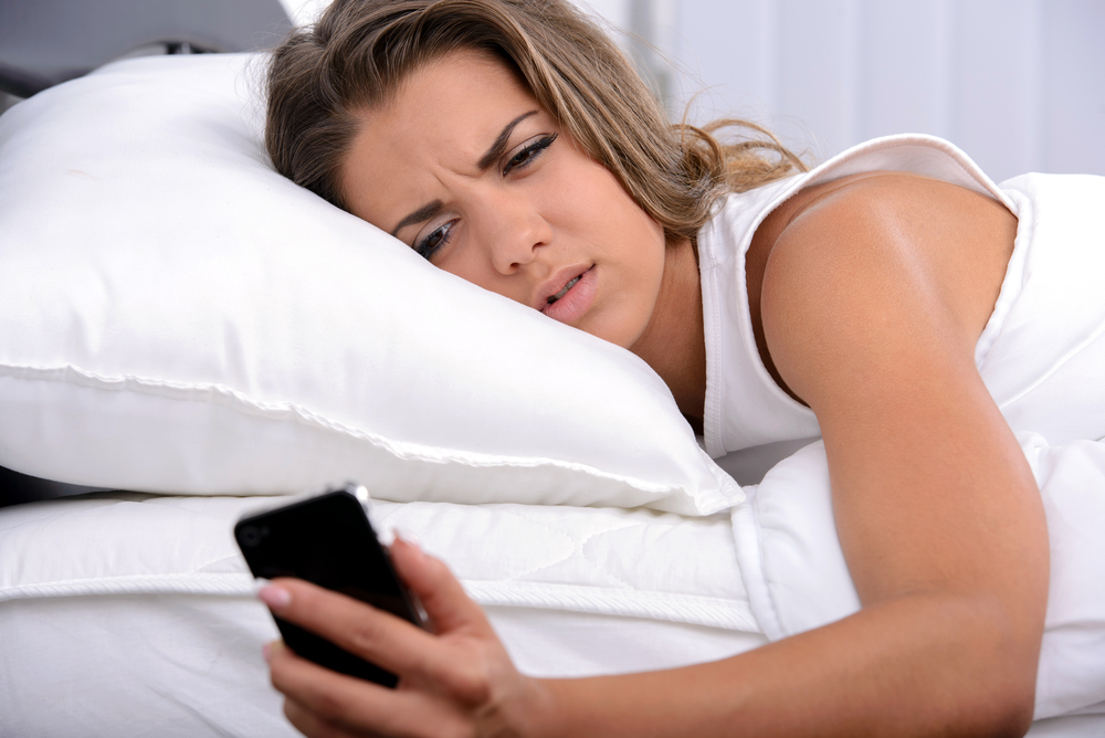 Woman lying on bed looking unhappy with a text message