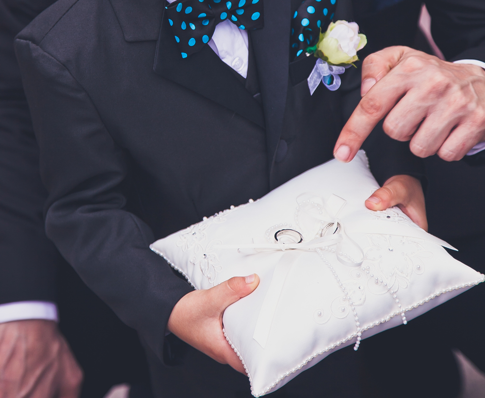 Young boy carrying wedding rings on a pillow during wedding ceremony